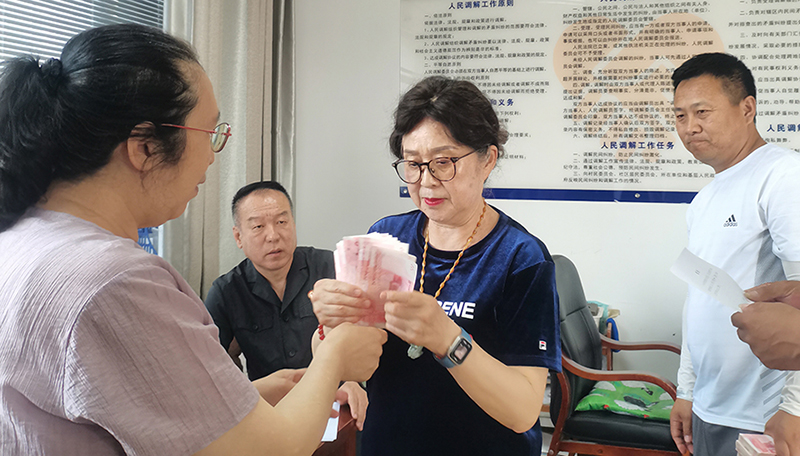 頭題片，5月30日，某藥業(yè)公司按協(xié)議約定完成第一期履行義務(wù)，將十萬現(xiàn)金交到法院，調(diào)解員付菊（左一）清點(diǎn)無誤之后交到農(nóng)民工委托代理人徐某手中