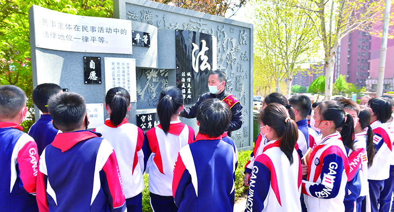 頭題圖，普法志愿者在憲法墻前給學(xué)生們普及法律知識(shí)。